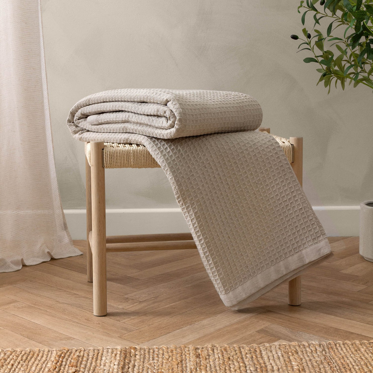 Canopy Plain Cotton Throw in natural, cotton waffle weave with plain border, draped over a wooden stool in a room with woven rug and curtain.
