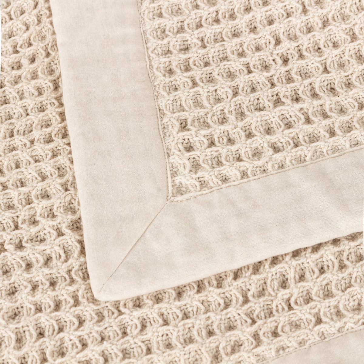 Close-up of the Canopy Plain Cotton Throw in natural beige, showing a chunky waffle weave centre with a wide plain cotton border and mitred corner detail.