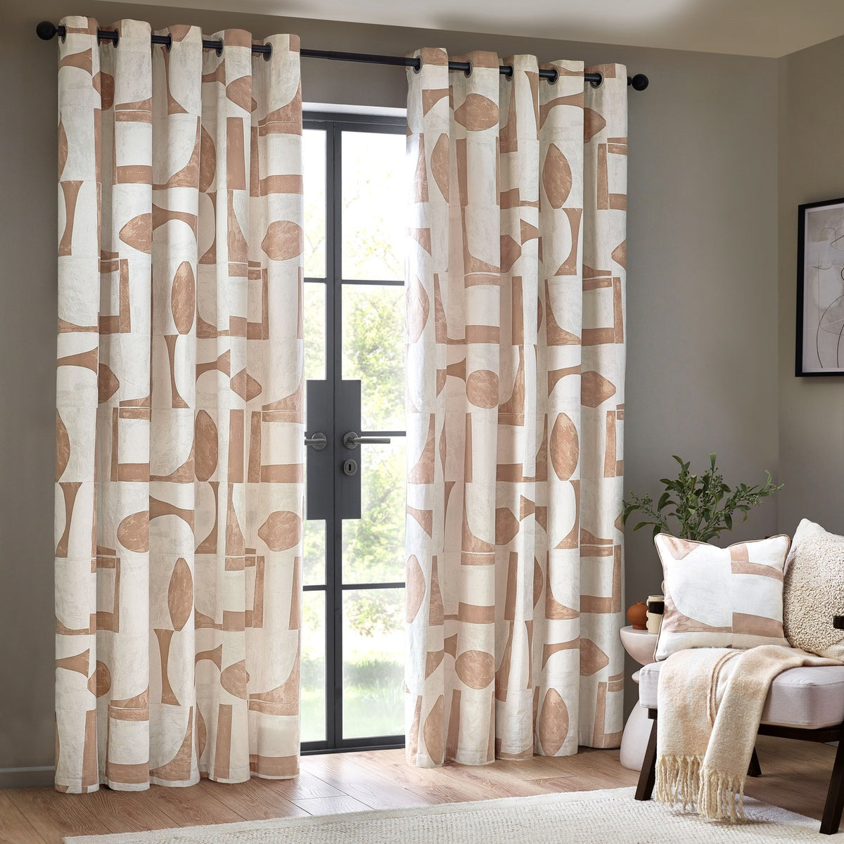 Carro Abstract Lined Eyelet Curtains in Clay, cream cotton panels with clay-toned geometric shapes on black eyelet rings, shown framing a glass door in a living room.