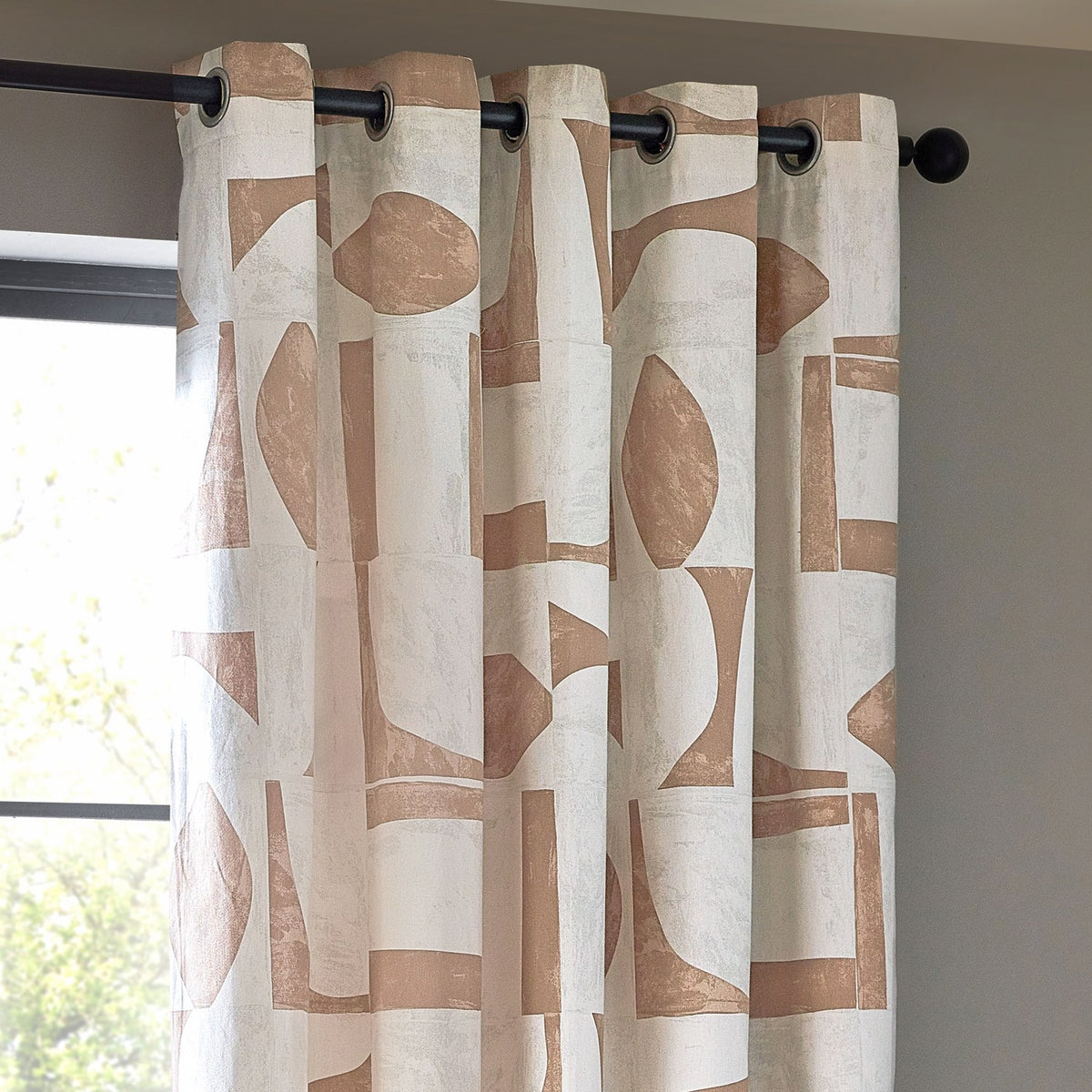 Carro Abstract Lined Eyelet Curtains in Clay, cream fabric with clay-toned geometric shapes, black eyelet rings on a black pole, hung by a window.