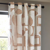 Carro Abstract Lined Eyelet Curtains in Clay, cream fabric with clay-toned geometric shapes, black eyelet rings on a black pole, hung by a window.