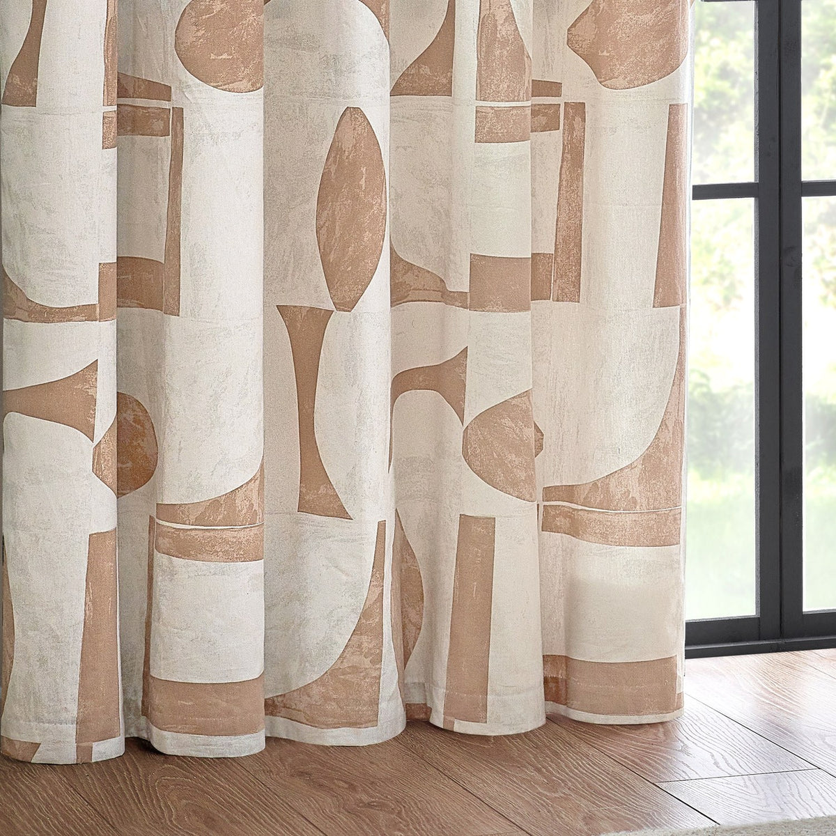 Carro eyelet curtain in clay, showing a cream cotton panel with abstract clay-toned geometric shapes, hung beside a window with a wooden floor.