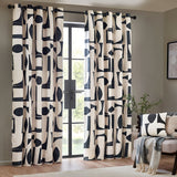 Carro Abstract Lined Eyelet Curtains in Dusk, cream cotton panels with bold black geometric shapes, hung on a black rod beside a glass door in a living room.