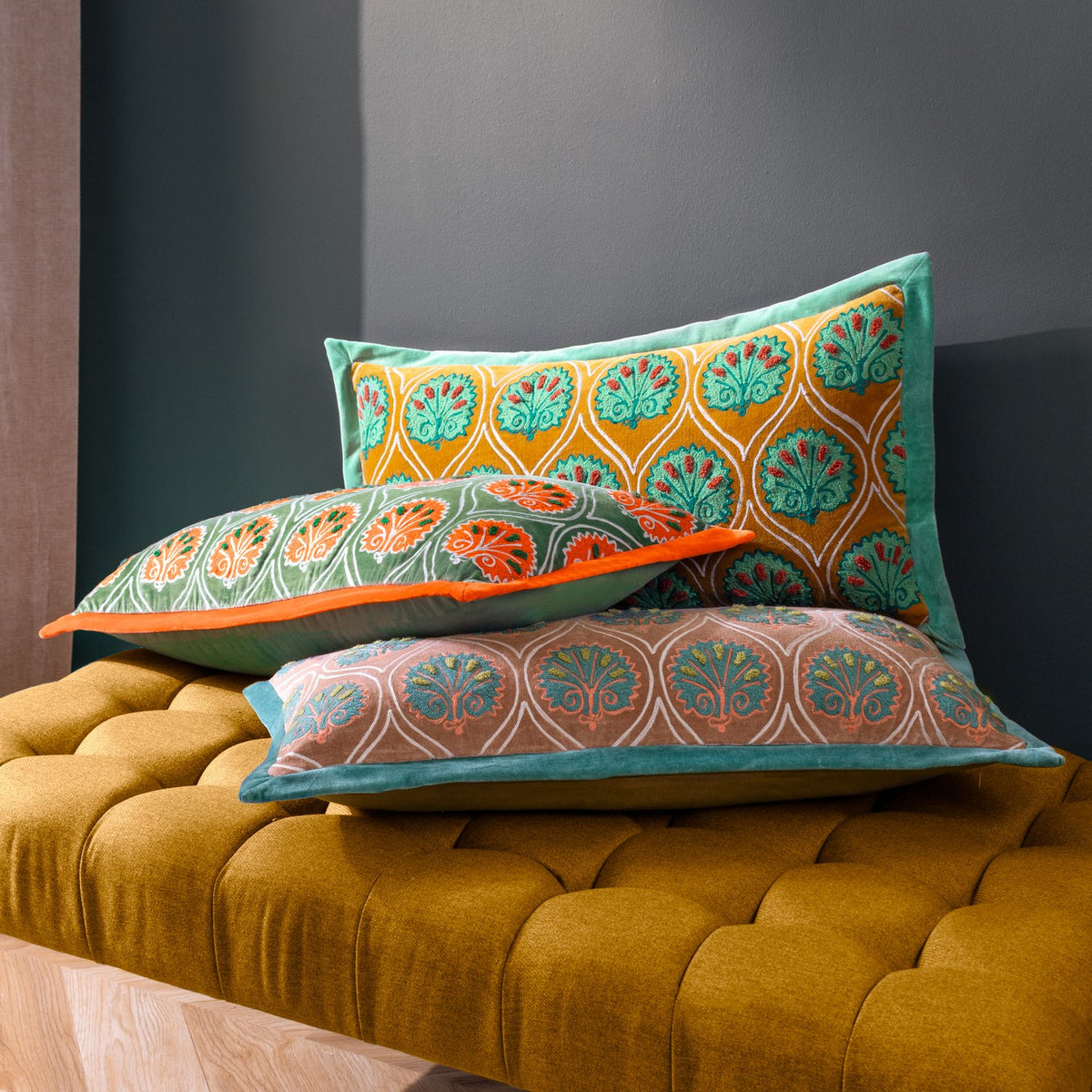 Casa Velvet Cotton Cushion in Rose/French Blue, embroidered teal frond pattern on dusky rose velvet with blue trim, styled with patterned cushions on a mustard velvet bench.