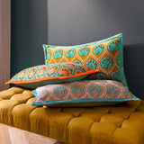 Casa Velvet Cotton Cushion in Rose/French Blue, embroidered teal frond pattern on dusky rose velvet with blue trim, styled with patterned cushions on a mustard velvet bench.
