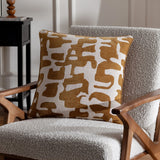 Caval Velvet Chenille Cushion in bronze, square with abstract jacquard shapes on a cream ground, shown on a boucle armchair in a living room setting.