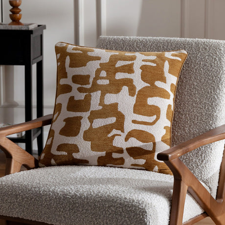 Caval Velvet Chenille Cushion in bronze, square with abstract jacquard shapes on a cream ground, shown on a boucle armchair in a living room setting.