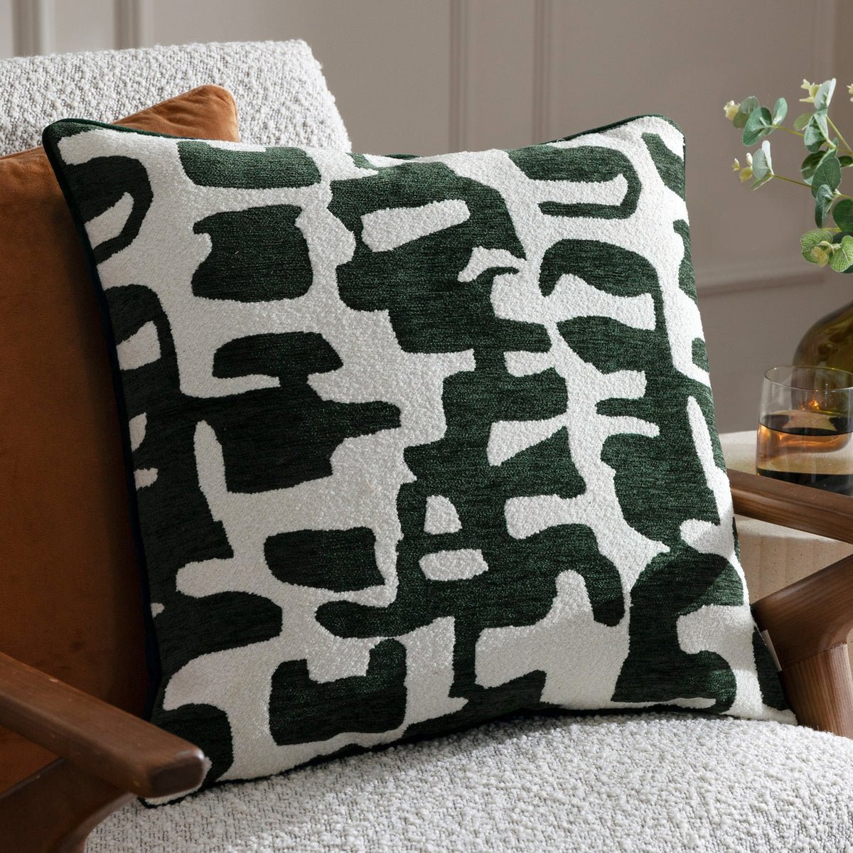 Caval Velvet Chenille Cushion in Ivy Green, square with an abstract jacquard pattern in dark green on off-white, textured chenille and boucle finish, shown on a light armchair.