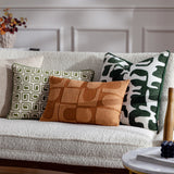 Caval Velvet Chenille Cushion in Ivy Green with abstract jacquard pattern, shown on a boucle sofa alongside patterned green and rust cushions.