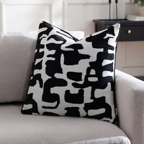 Caval Velvet Chenille Cushion in Mono, a square 50x50cm cushion with an abstract black jacquard pattern on an off-white ground, shown on a light grey sofa.