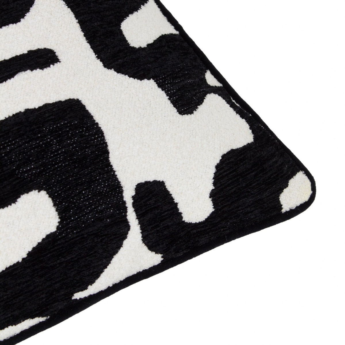 Close-up corner of the Caval Velvet Chenille Cushion in Mono, showing black abstract jacquard shapes on an off-white ground with a black piped edge.
