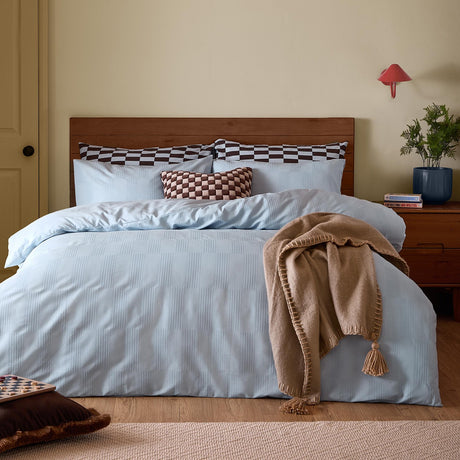Club Checkerboard Plain Check Duvet Cover Set in Blueberry on a bed with wooden headboard, styled with checkerboard pillows and a tan tasselled throw in a bedroom setting.