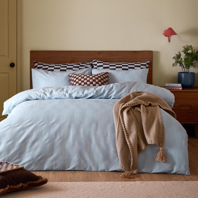 Club Checkerboard Plain Check Duvet Cover Set in Blueberry on a bed with wooden headboard, styled with checkerboard pillows and a tan tasselled throw in a bedroom setting.