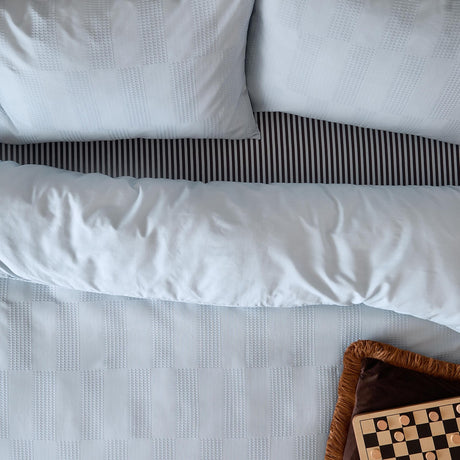Club Checkerboard Plain Check Duvet Cover Set in Blueberry, pale blue waffle-textured bedding with pillowcases and black striped trim, styled with a checkers board on a bed.