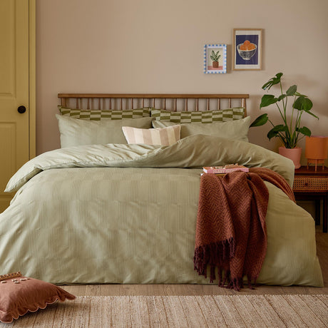 Club Checkerboard duvet cover set in green on a bed with matching pillowcases, a striped cushion, and a rust-coloured throw in a bedroom setting.