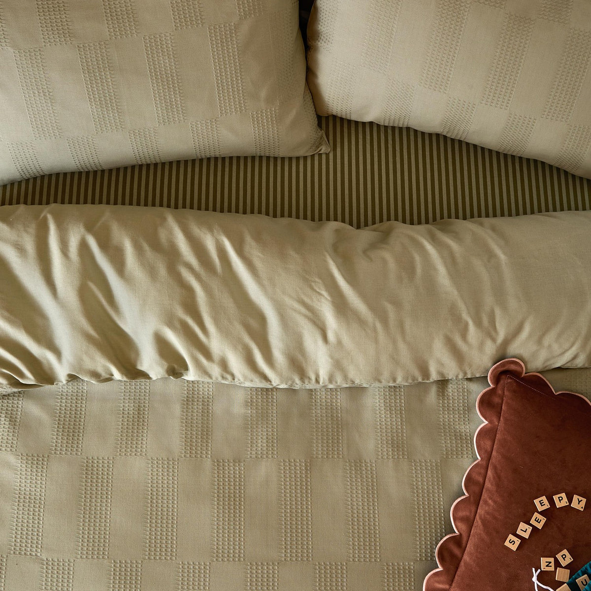 Club Checkerboard duvet cover set in green, showing waffle-textured checkerboard pillowcases, striped edging, and a folded bolster on a checked duvet cover.