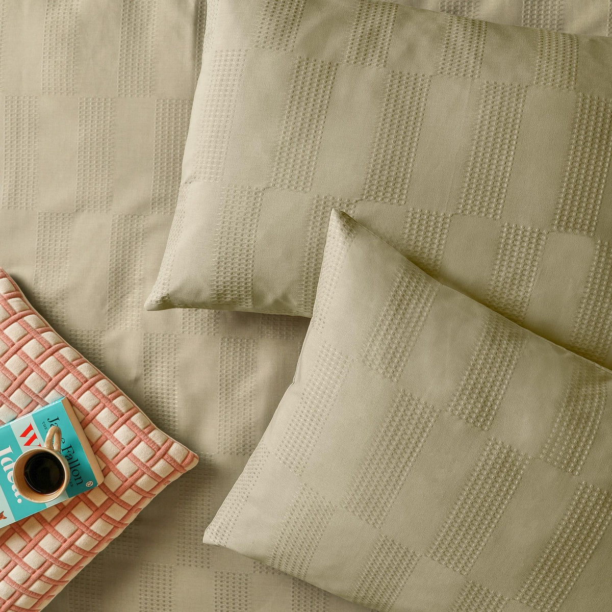 Green Club Checkerboard duvet cover set with waffle-textured pillowcases showing a woven check pattern, styled with a coral geometric cushion and coffee cup.