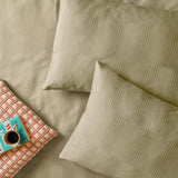 Green Club Checkerboard duvet cover set with waffle-textured pillowcases showing a woven check pattern, styled with a coral geometric cushion and coffee cup.