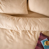 Club Checkerboard duvet cover set in latte, showing waffle-textured squares on the duvet and pillowcases with a striped reverse, styled on a bed with a book and mug.