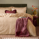 Club Checkerboard duvet cover set in latte with waffle-textured checkerboard design, styled on a bed with matching pillowcases, a burgundy velvet cushion, and a herringbone throw.