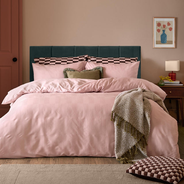 Pink checkerboard duvet cover set on a bed with teal headboard, styled with matching pillowcases, olive cushions and a herringbone throw.