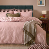 Club Checkerboard duvet cover set in Pink Smoothie on a bed with checkerboard pillowcases, green cushions, and a herringbone throw in a bedroom setting.