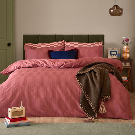 Club Checkerboard duvet cover set in raspberry pink with waffle-textured check pattern, styled on a bed with navy cushion and brown fringed throw in a bedroom setting.