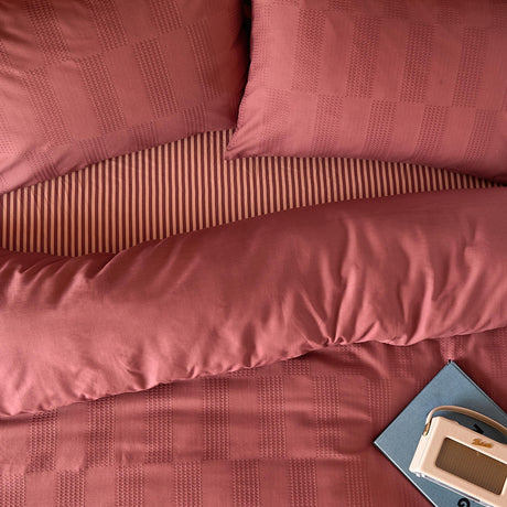 Club Checkerboard Duvet Cover Set in raspberry pink, showing a waffle-textured check pattern on pillowcases and striped cotton-blend cover, styled with a radio and book.