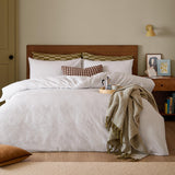 Club Checkerboard duvet cover set in white waffle-textured cotton-polyester blend, styled on a bed with checked pillowcases, a patterned cushion, and an olive throw in a bedroom setting.