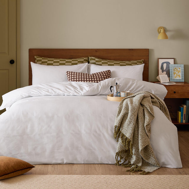 Club Checkerboard duvet cover set in white waffle-textured cotton-polyester blend, styled on a bed with checked pillowcases, a patterned cushion, and an olive throw in a bedroom setting.