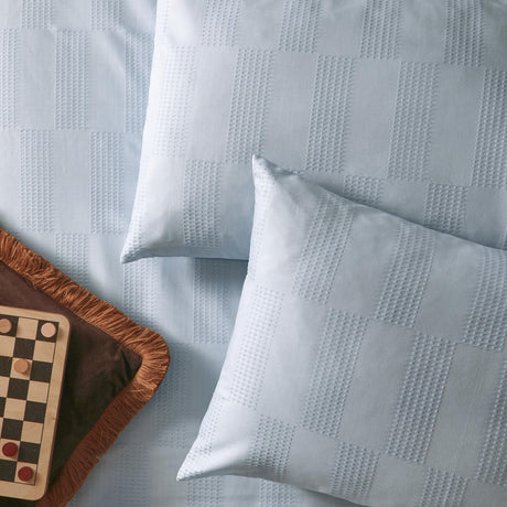Club Checkerboard cotton blend pillowcase pair in Blueberry, shown on a bed with woven waffle-textured checkerboard pattern and smooth reverse, styled beside a checkers board.