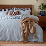 Club Checkerboard cotton blend pillowcase pair in blueberry blue, styled on a bedroom bed with matching checked cushion and camel throw against a wooden headboard.