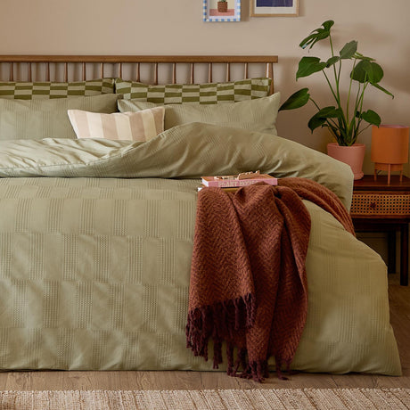 Club Checkerboard Cotton Blend Pillowcase Pair in green on a bed with olive checkerboard duvet, striped cushions, and a rust throw, set in a bedroom.