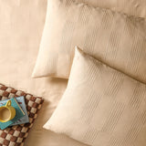 Club Checkerboard Cotton Blend Pillowcase Pair in Latte, shown on a bedroom bed with matching duvet, waffle-textured checkerboard weave, styled beside a checked tray and yellow mug.