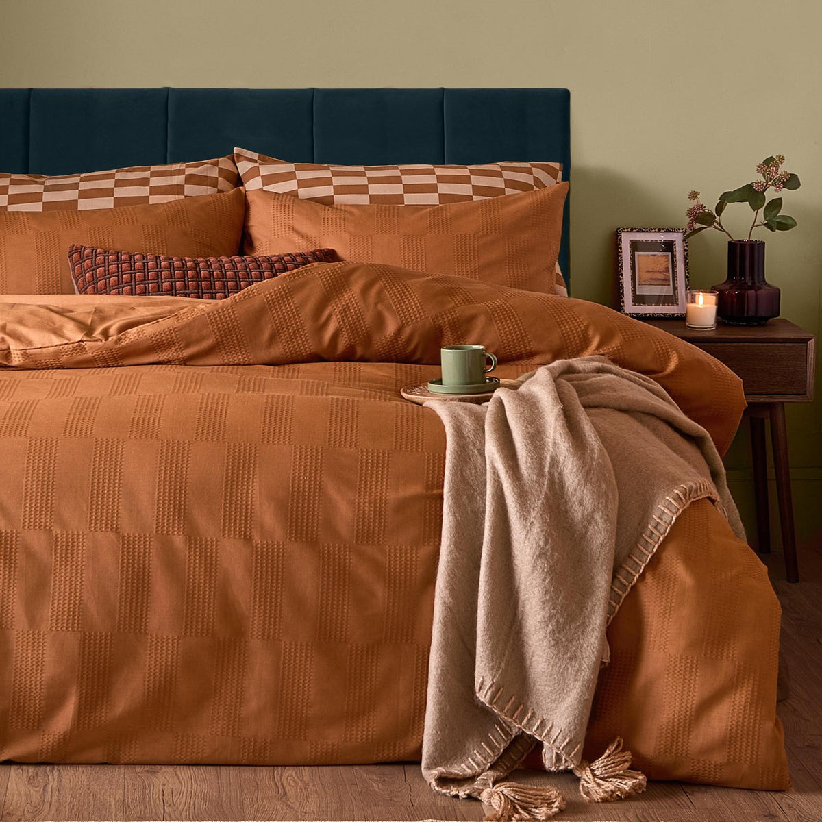 Club Checkerboard cotton blend pillowcase pair in pumpkin orange with waffle-textured checkerboard pattern, styled on a bed with matching duvet cover in a bedroom setting.