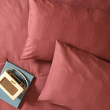 Club Checkerboard cotton blend pillowcase pair in raspberry red with woven waffle-texture check design, styled on a bed with a vintage radio and book.
