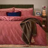 Bedroom scene with Club Checkerboard cotton blend pillowcase pair in raspberry red, checkerboard pattern on bed styled with pink duvet and a brown blanket.
