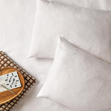 Club Checkerboard cotton blend pillowcase pair in white with a woven waffle check texture, styled on a bed with a wooden tray and crossword puzzle.