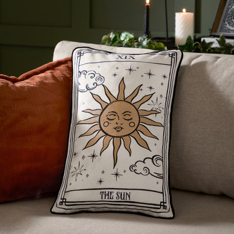 Celestial Stories Linen Cotton Cushion in cream and black, embroidered tarot-style Sun card design with sun face, stars and clouds, shown on a sofa.