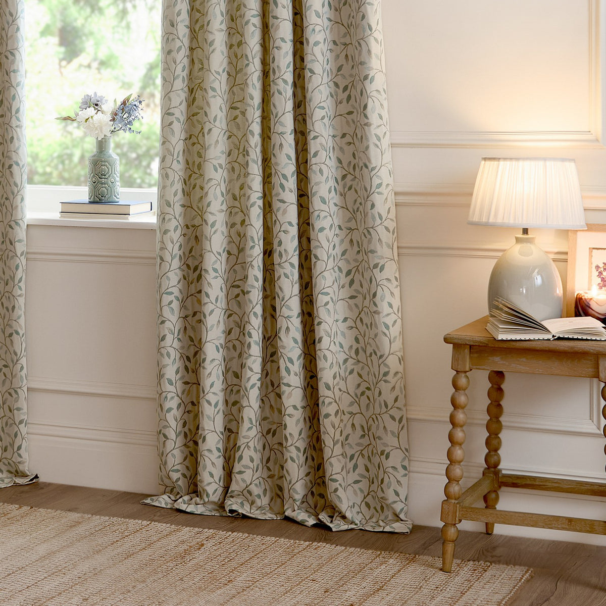 Cervino Jacquard Pencil Pleat Curtains in Duck Egg, cream fabric with woven trailing leaf pattern in blue, sage and tan, shown pooling by a window in a living room setting.