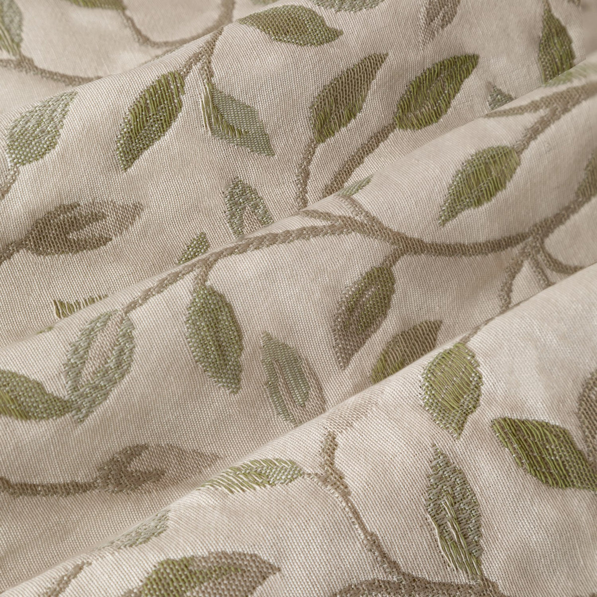 Cervino pencil pleat curtain fabric close-up in cream polyester with jacquard trailing leaf design in muted green and taupe tones, showing textured woven detail.