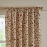 Cervino pencil pleat curtains in cream jacquard fabric with woven leaf and stem pattern in rust, terracotta, pink and green, shown pleated on a wooden pole by a window.