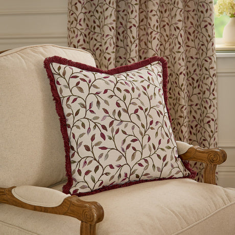 Cervino Jacquard Cotton Blend Cushion in Damson with red fringe trim, cream ground and leafy trailing pattern in wine, pink and green tones, shown on a beige armchair.