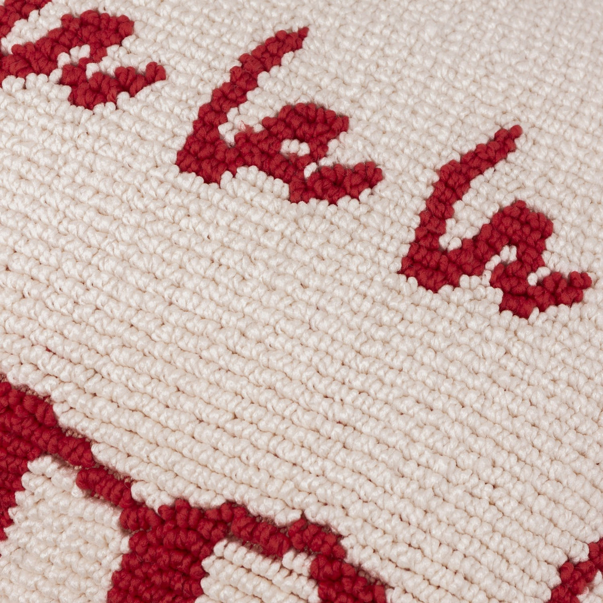Close-up of the Candy Fa La La cushion showing red hand-tufted "Fa La" lettering on a cream cotton-polyester looped pile face.