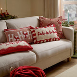 Candy Fa La La cushion in cream with a hand-tufted "Fa la la la" motif and red-and-white candy-stripe border, shown centre stage among festive cushions on a sofa.