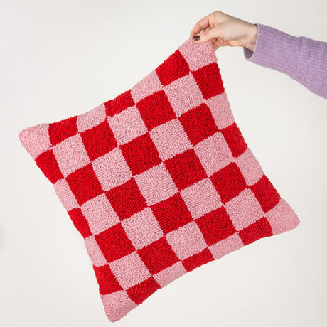 Check Knitted Polycotton Cushion in red and pink checkerboard, held by hand against a plain white background, showing the tufted loop-pile texture.
