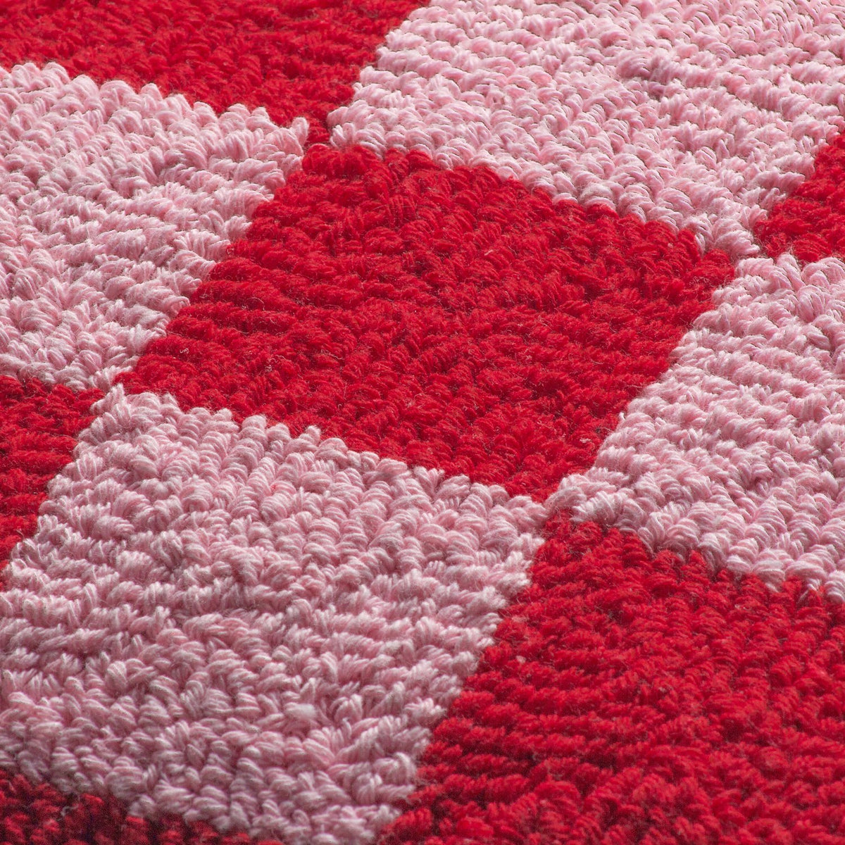 Close-up of the Check Knitted Polycotton Cushion in Red or Dead Pink, showing the raised loop-tufted checkerboard texture in alternating red and pink squares.