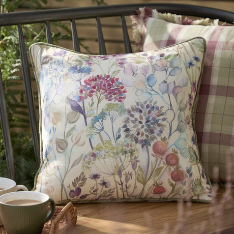 Country Hedgerow Reversible Linen Cushion in Moss, 45x45cm, floral watercolour side shown with green piping, styled on an outdoor bench beside checked cushions.