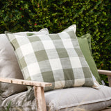Chesil Check Printed Cotton Cushion in moss green and off-white buffalo check with flat oxford edge, shown on a grey sofa against outdoor greenery.