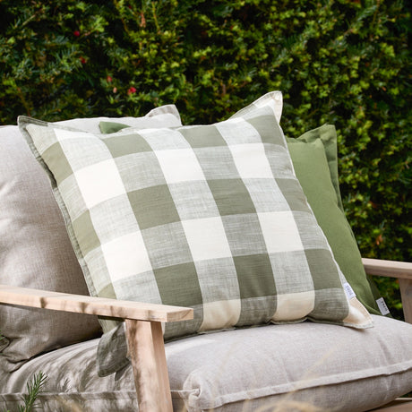 Chesil Check Printed Cotton Cushion in moss green and off-white buffalo check with flat oxford edge, shown on a grey sofa against outdoor greenery.